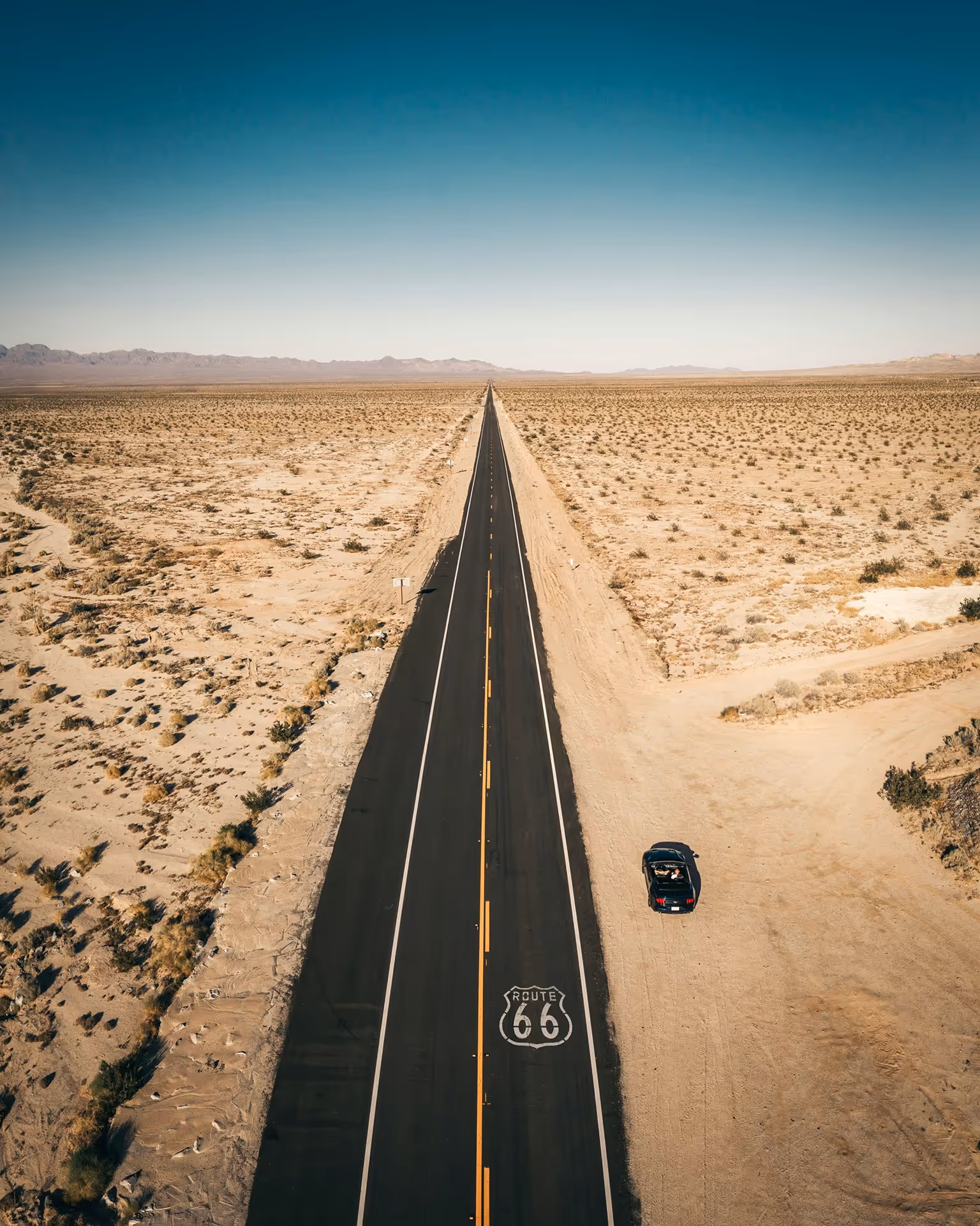 Lone car driving on empty Route 66 through desert landscape