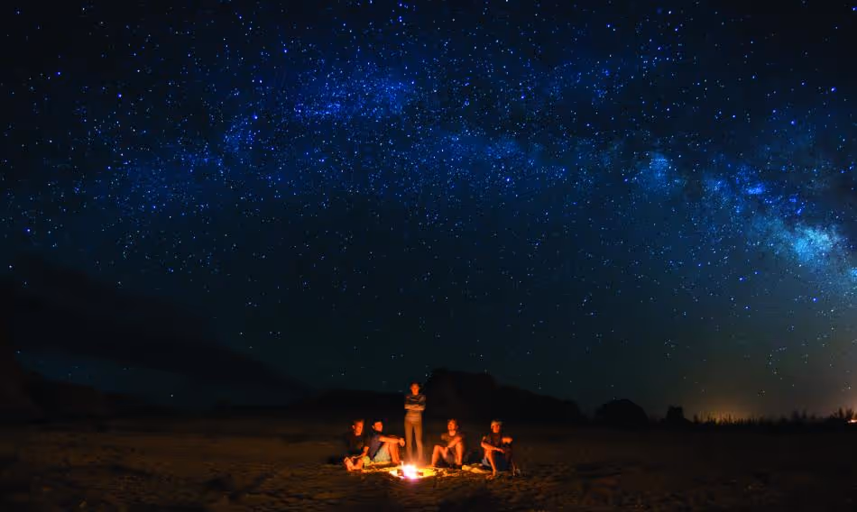 Campfire under vibrant Milky Way galaxy on dark starry night