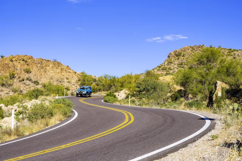 Blue SUV driving on winding desert road through rocky landscape