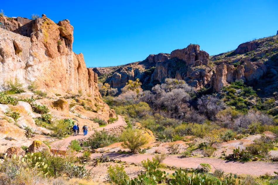 Hikers walking on desert trail among rocky cliffs and cacti