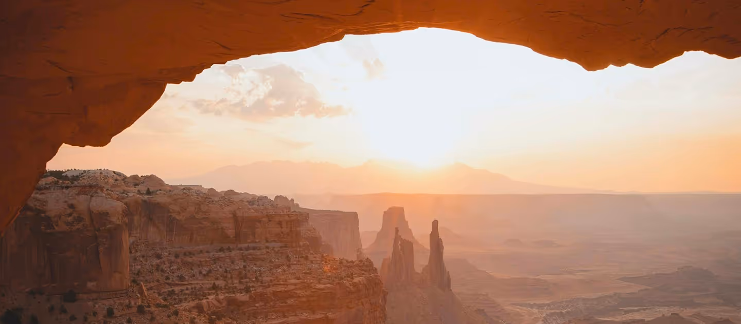 Sunrise over desert canyon with rock formations viewed through stone arch