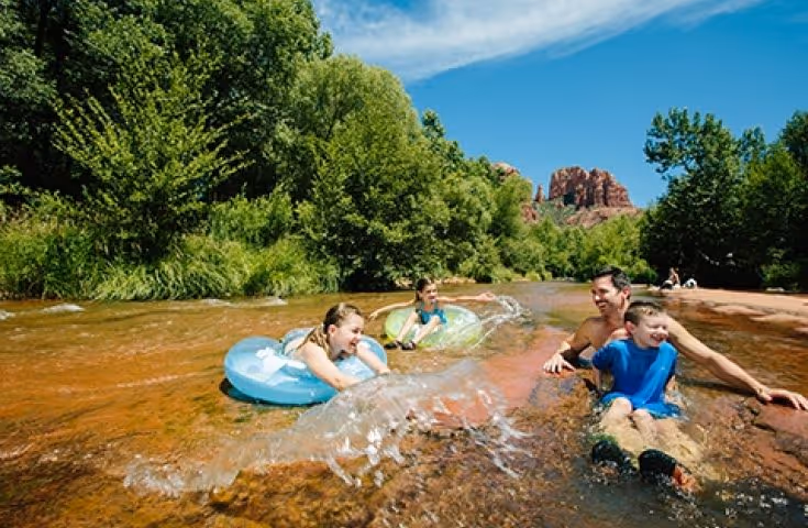 Family playing in river with inner tubes near red rock formation