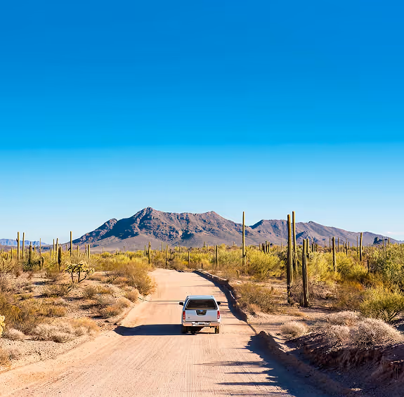 Truck driving on desert road with saguaro cacti and mountain backdrop