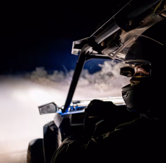 Off-road vehicle driver in helmet navigating through dusty terrain at night