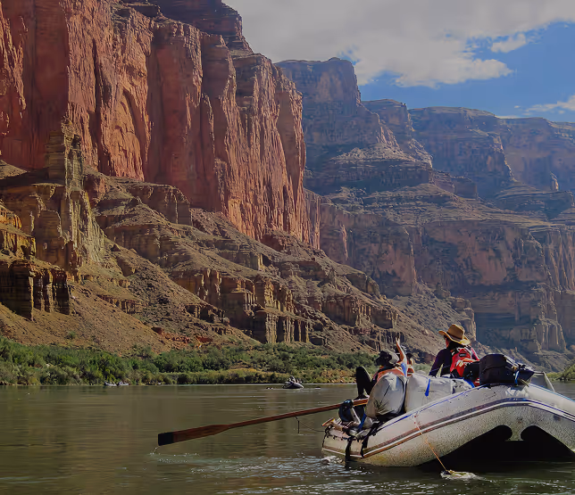 Rafting down river with towering red rock canyon walls in background