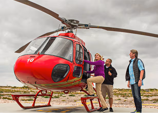 Red helicopter with people preparing to board on rocky terrain