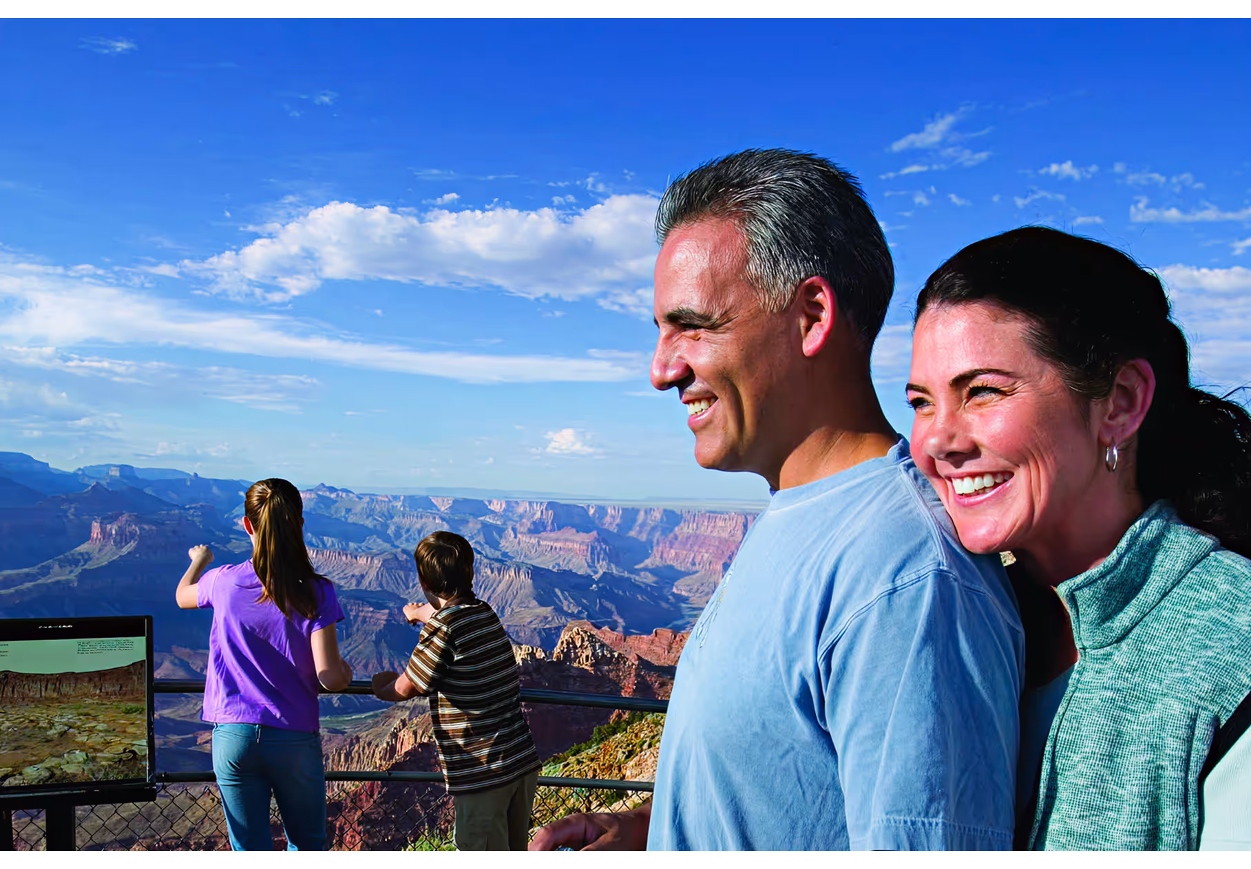 Couple smiling at Grand Canyon overlook with visitors in background