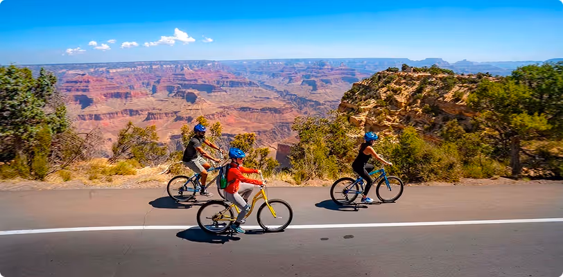 Cyclists riding bikes along scenic road with Grand Canyon in background