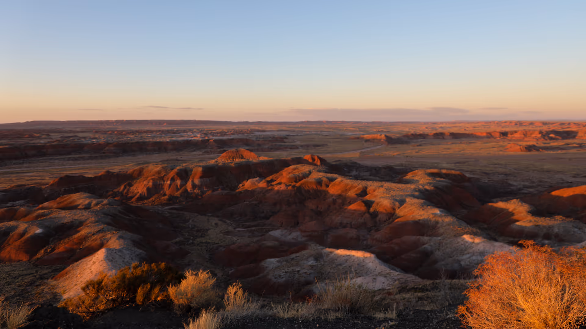 Sunlit rugged desert landscape with reddish and white rock formations under a clear sky at sunset.