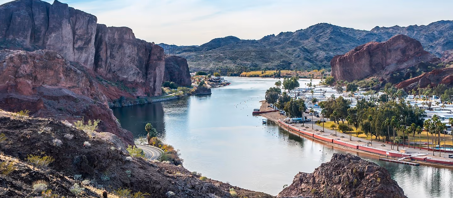 River flowing between rocky cliffs with a park and RV campground on the right shore under a clear sky.