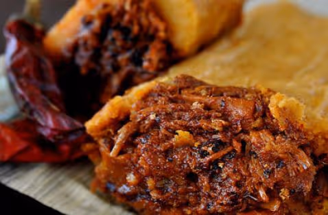 Close-up of a traditional meat tamale showing seasoned shredded meat filling and a red chili pepper on a banana leaf.