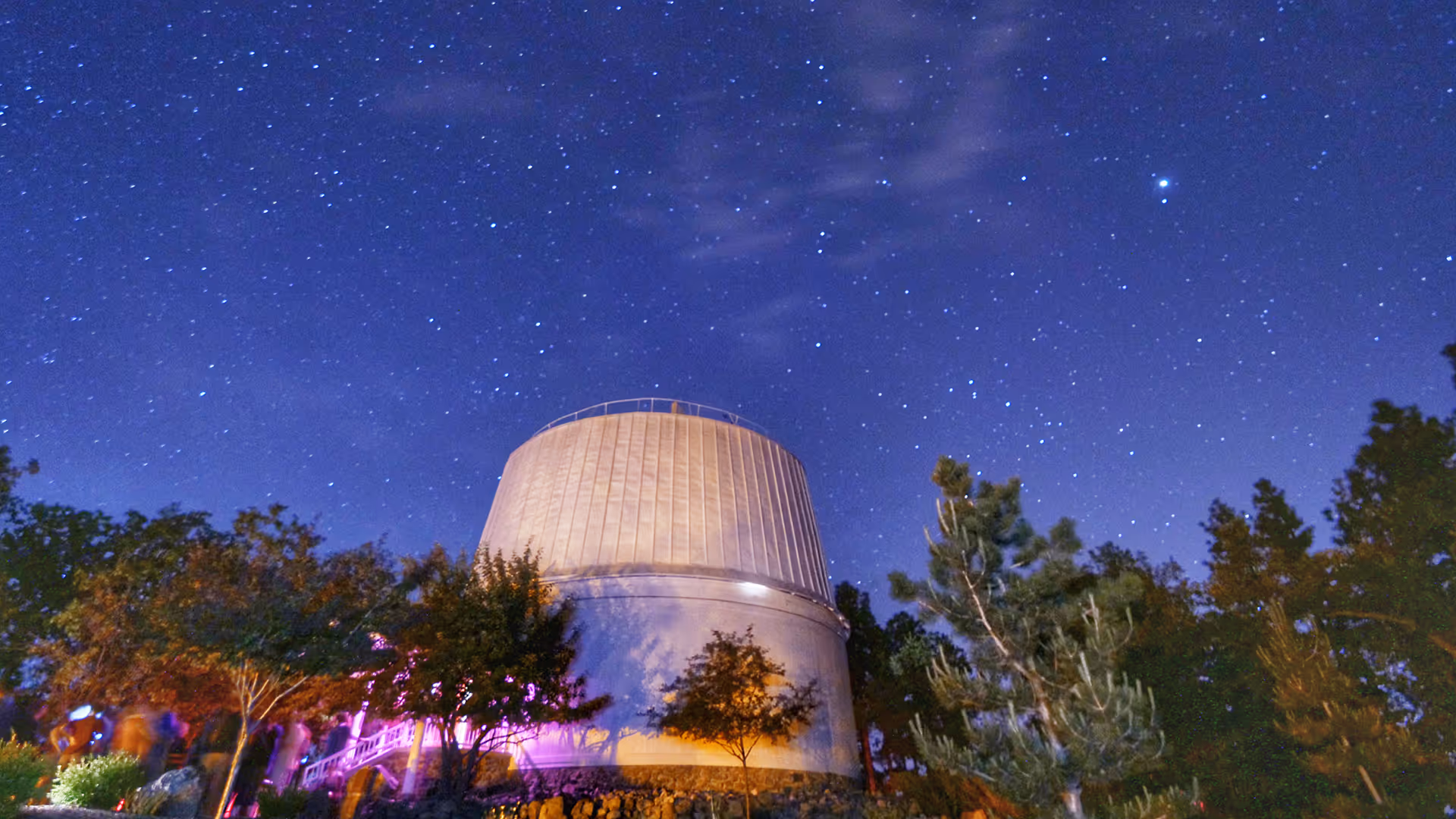 Lowell Observatory dome at night under a star-filled sky with trees surrounding the structure.