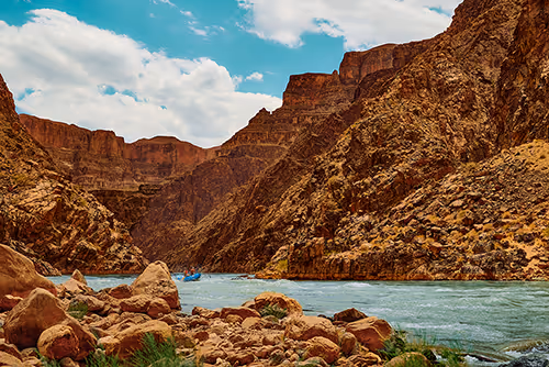 Clear river flowing through a rocky canyon with steep cliffs under a partly cloudy sky.