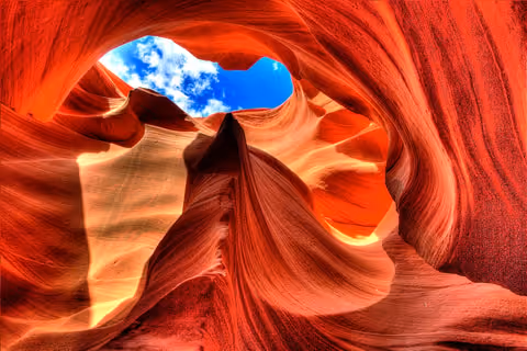 Curved orange and red sandstone formations inside Antelope Canyon with a bright blue sky visible through an opening above.