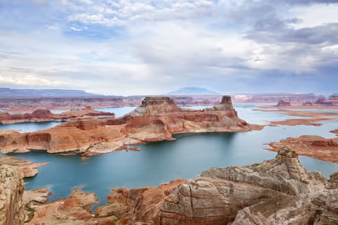 Scenic view of Lake Powell with turquoise water winding among red rock formations under a cloudy sky.