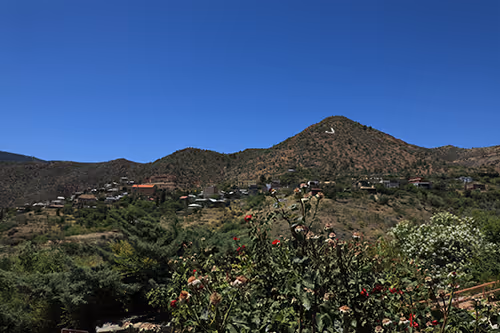 View of a hillside town with scattered houses, green vegetation in the foreground, and a clear blue sky.