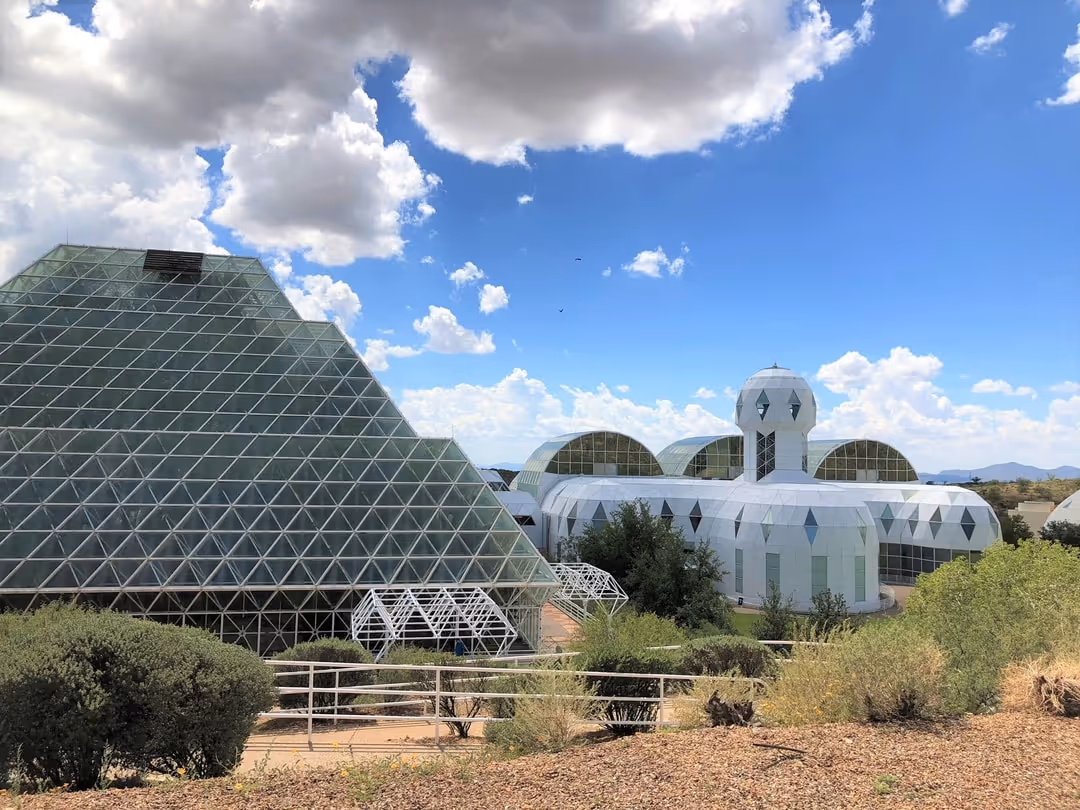 Biosphere 2 complex featuring large glass pyramid and white dome structures under a partly cloudy blue sky.