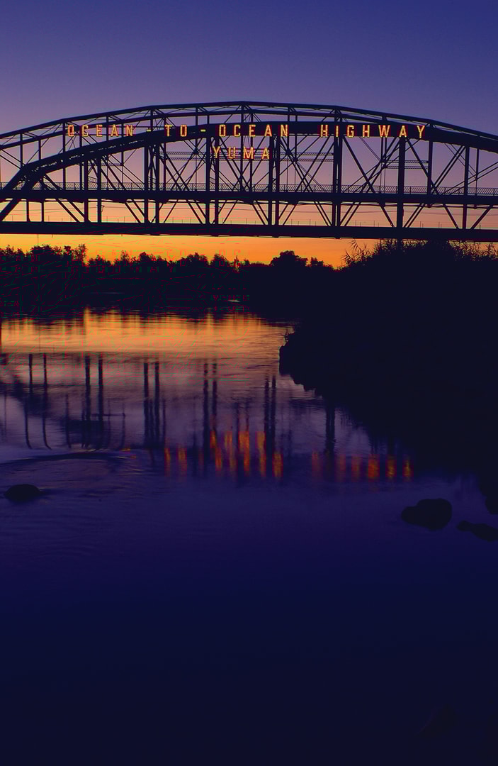 Silhouette of the Ocean to Ocean Highway bridge over a river at sunset with orange and purple sky reflecting in the water.