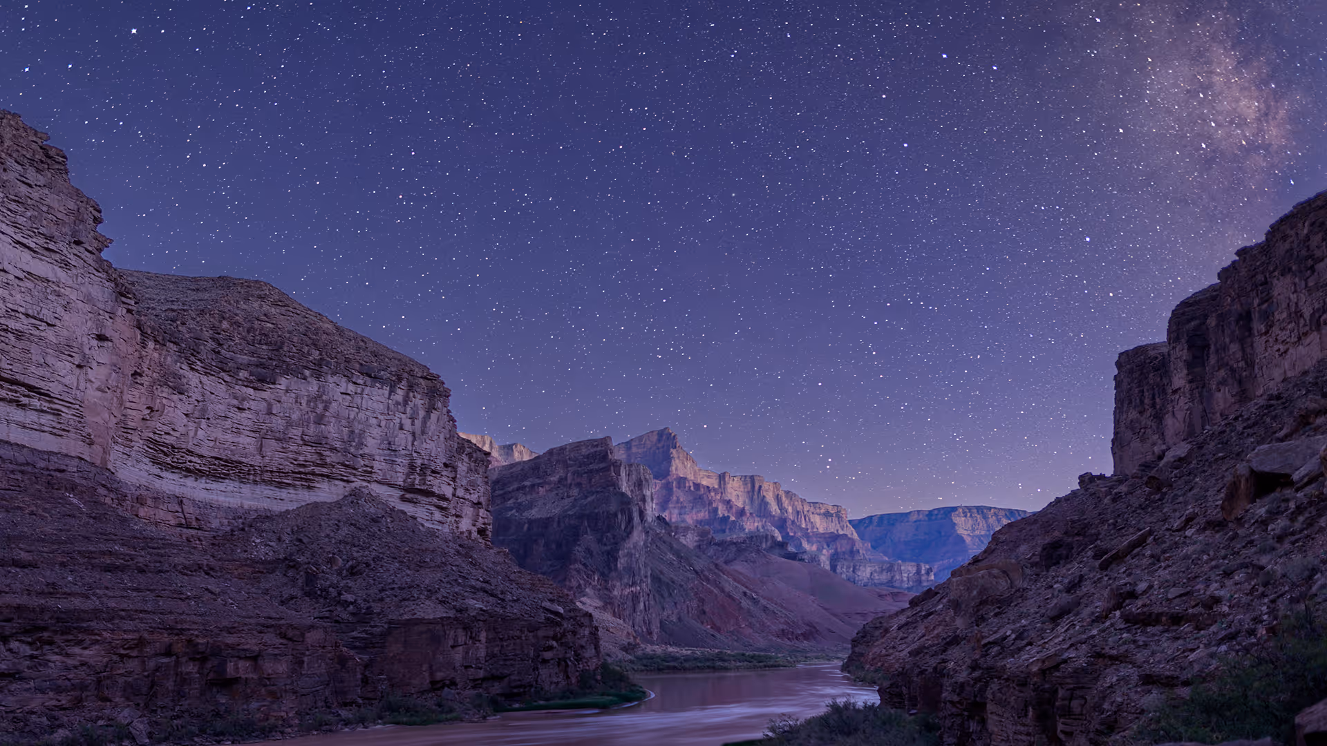 Starry night sky over the Grand Canyon with a river running through rocky cliffs.