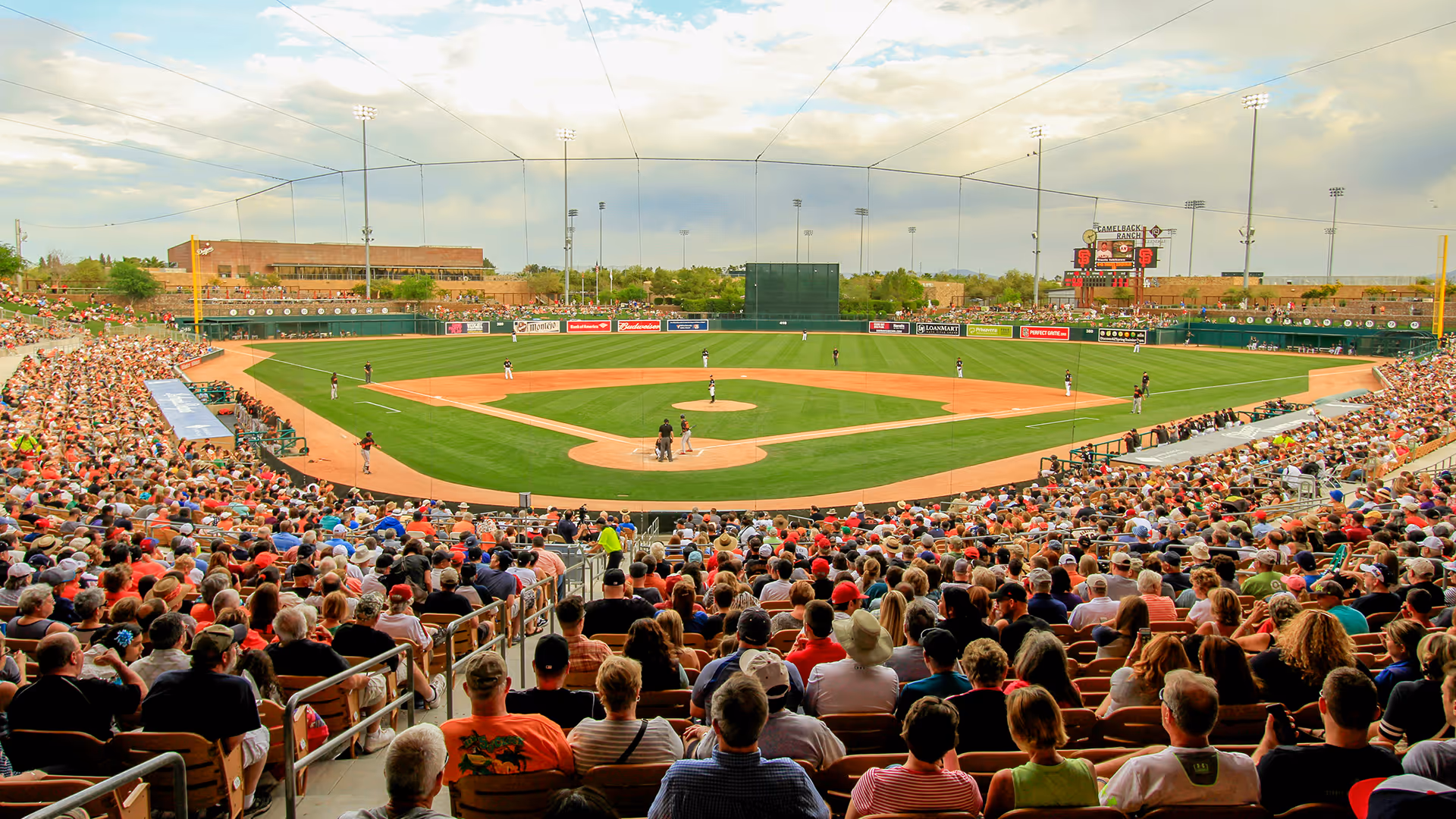 Crowded baseball stadium with players on field and scoreboard displaying Camelback Ranch home of Giants and White Sox.