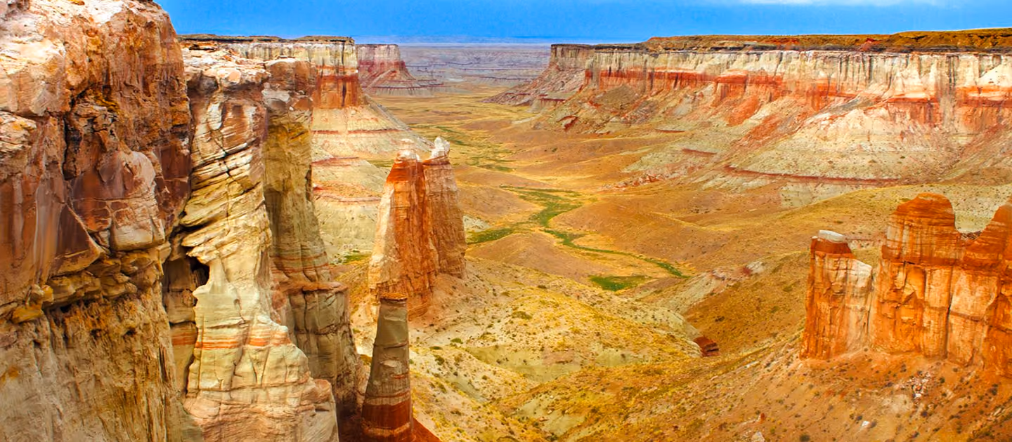 Wide canyon landscape with layered red and white rock formations under a clear blue sky.