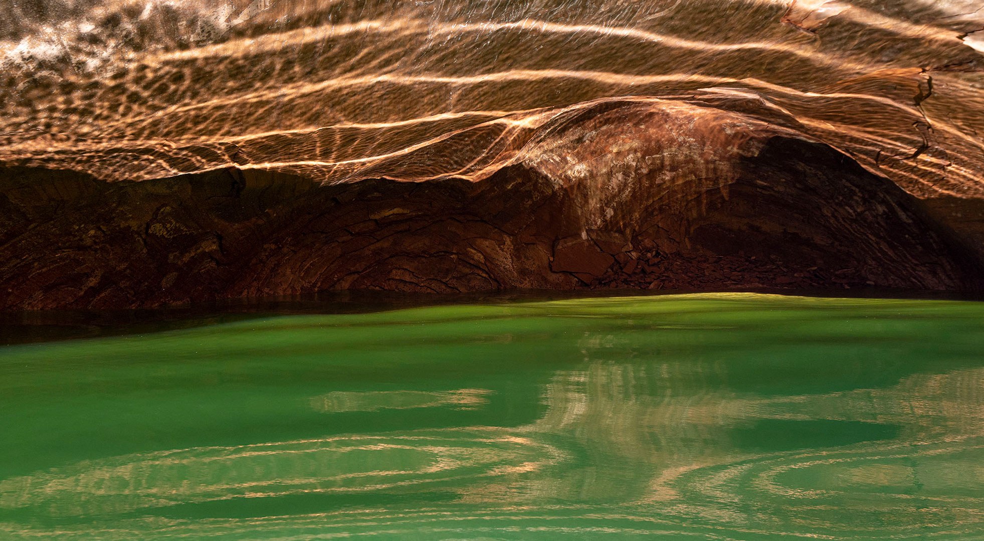In Reflection Canyon the sunlight plays off the emerald water casting shadows on the low canyon ceiling