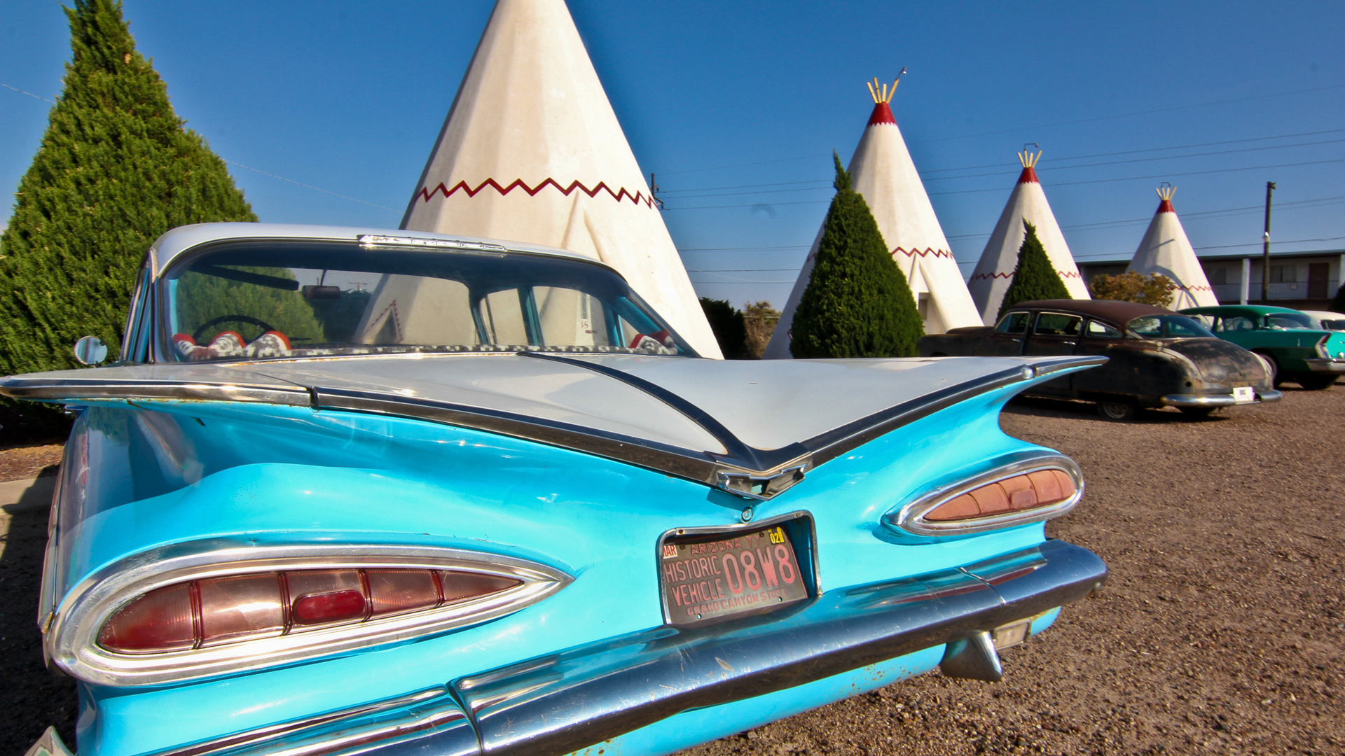 A vintage blue car is parked next to a white stucco wigwam along Route 66