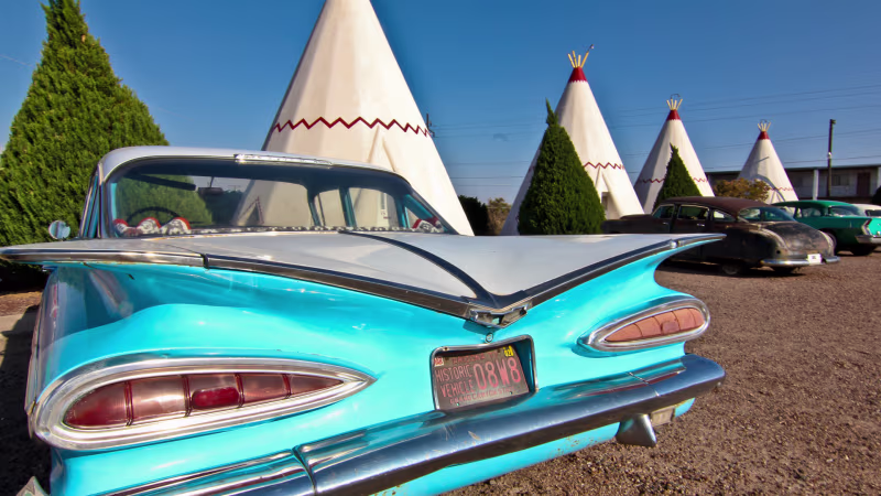 A vintage blue car is parked next to a white stucco wigwam along Route 66