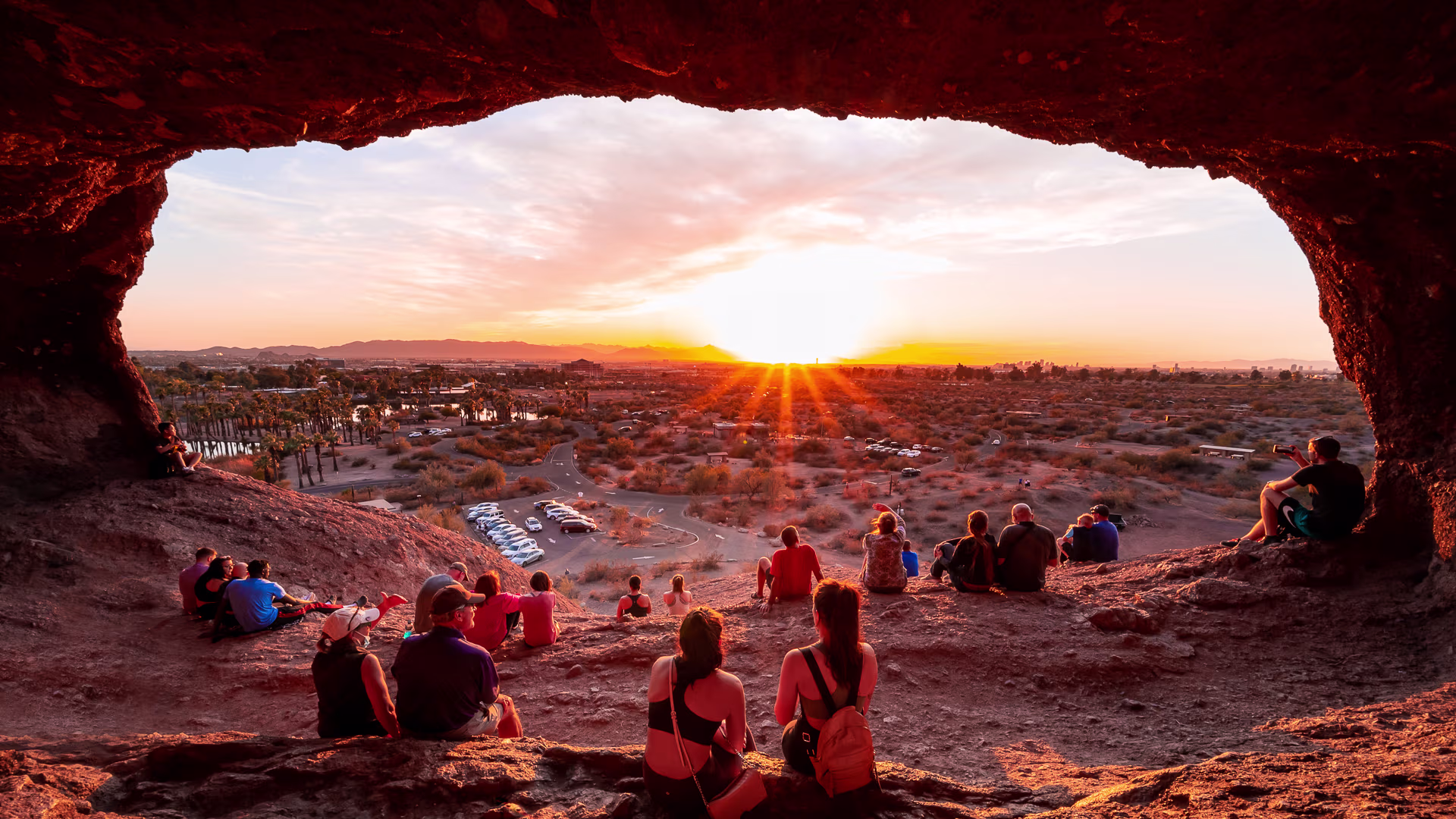 A red butte rises from the desert floor, surrounded by palm trees.