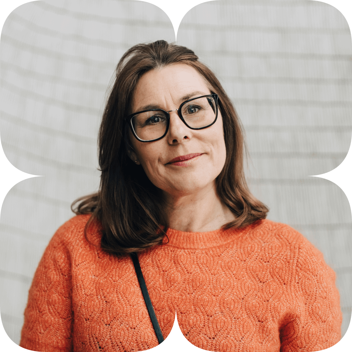 A person in a bright orange sweater stands in front of a  white brick wall looks to the left.