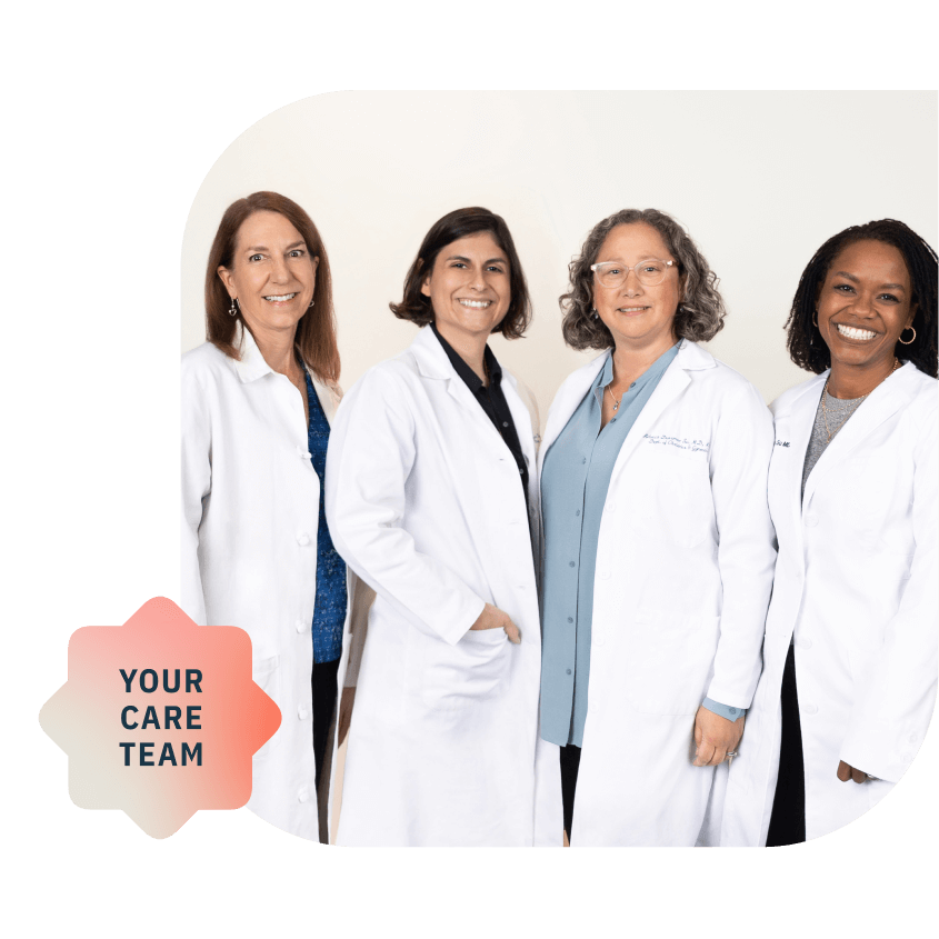 Four people stand together in white doctors coats, against a white wall, smiling at the camera.