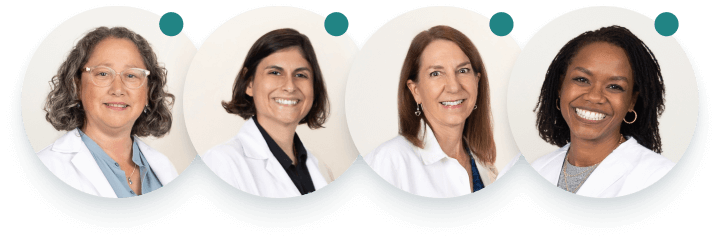 Four people stand together in white doctors coats, against a white wall, smiling at the camera.