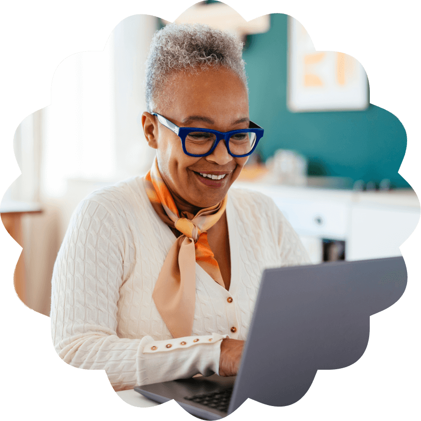 A person in a white blouse in a colored scarf, looks happily at their computer. 