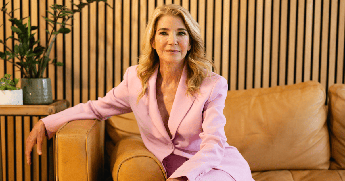 Candace Bushnell wears a pink suit while sitting on a couch