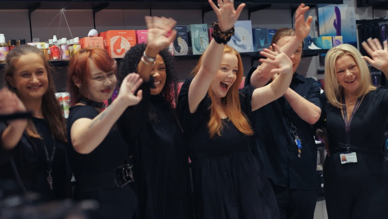 Ann Summers retail employees standing in front of product display and waving at the camera