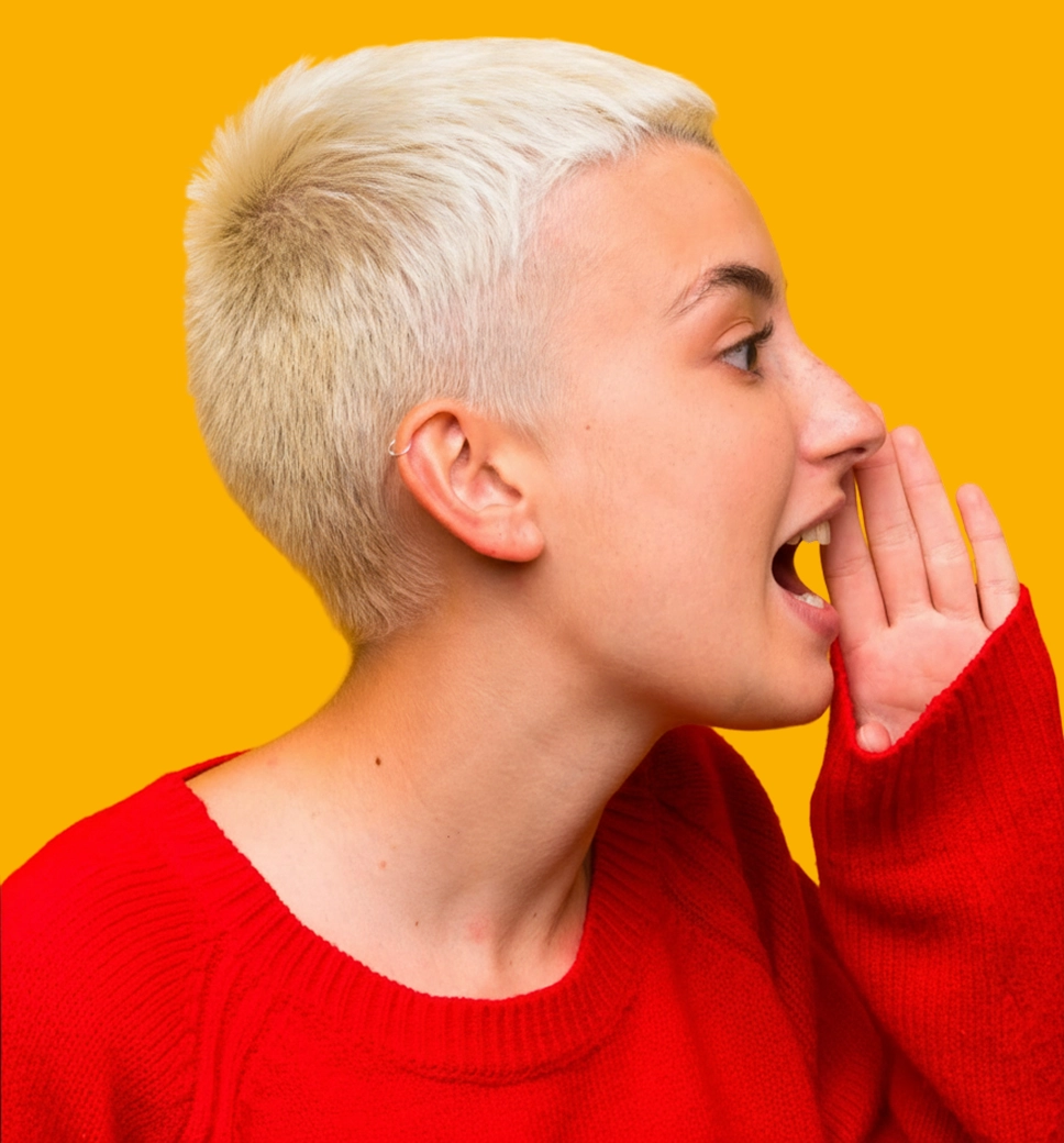 A profile shot of a person with short blonde hair and a red sweater, cupping their hand to their mouth as if whispering or shouting a secret, set against a solid yellow background.