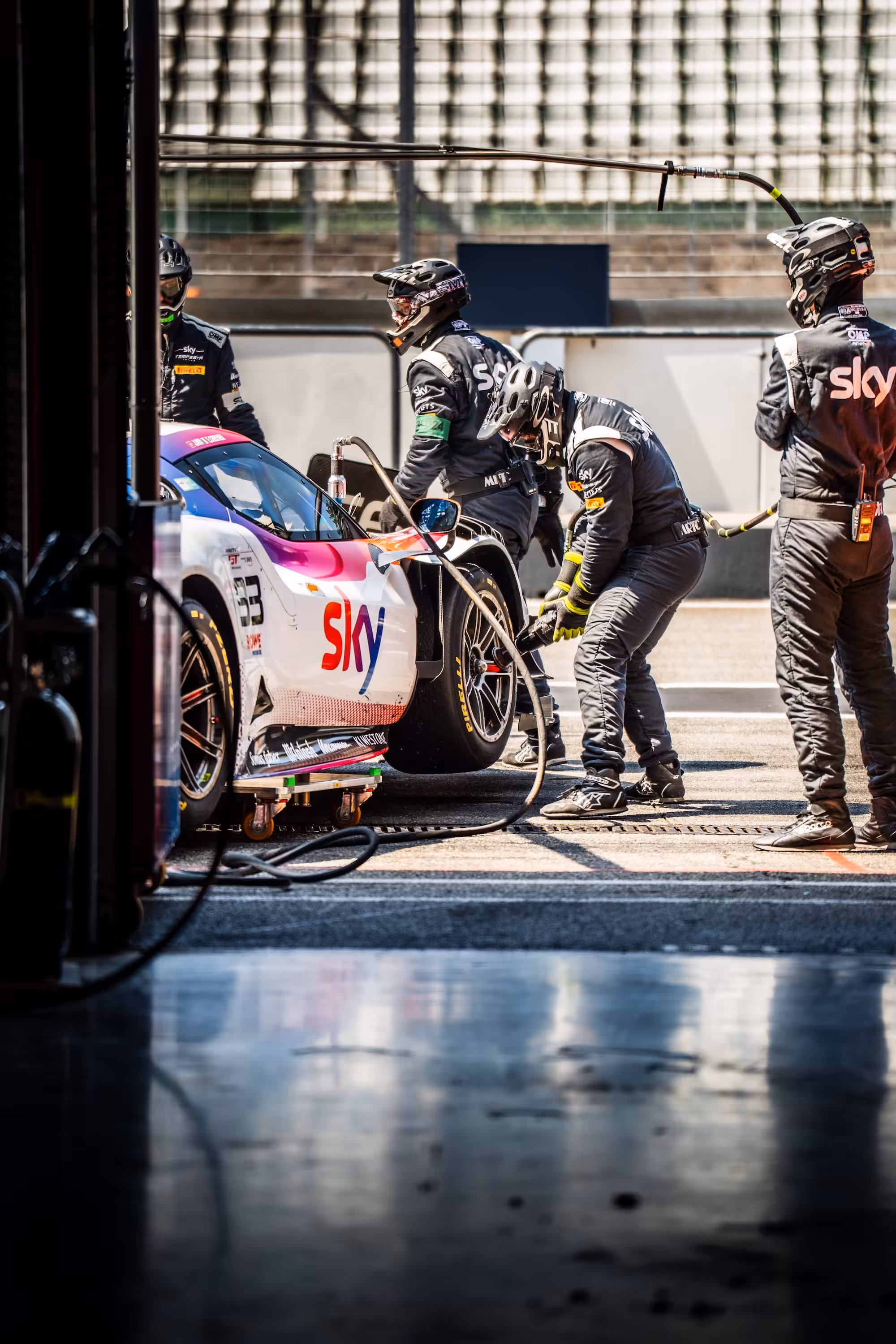 Boxenstopp des Sky Tempesta Racing Teams bei der FANATEC GT WORLD CHALLENGE 2024 am Hockenheimring. Mechaniker in schwarzen Anzügen und Helmen arbeiten in der Boxengasse am weißen Rennwagen.