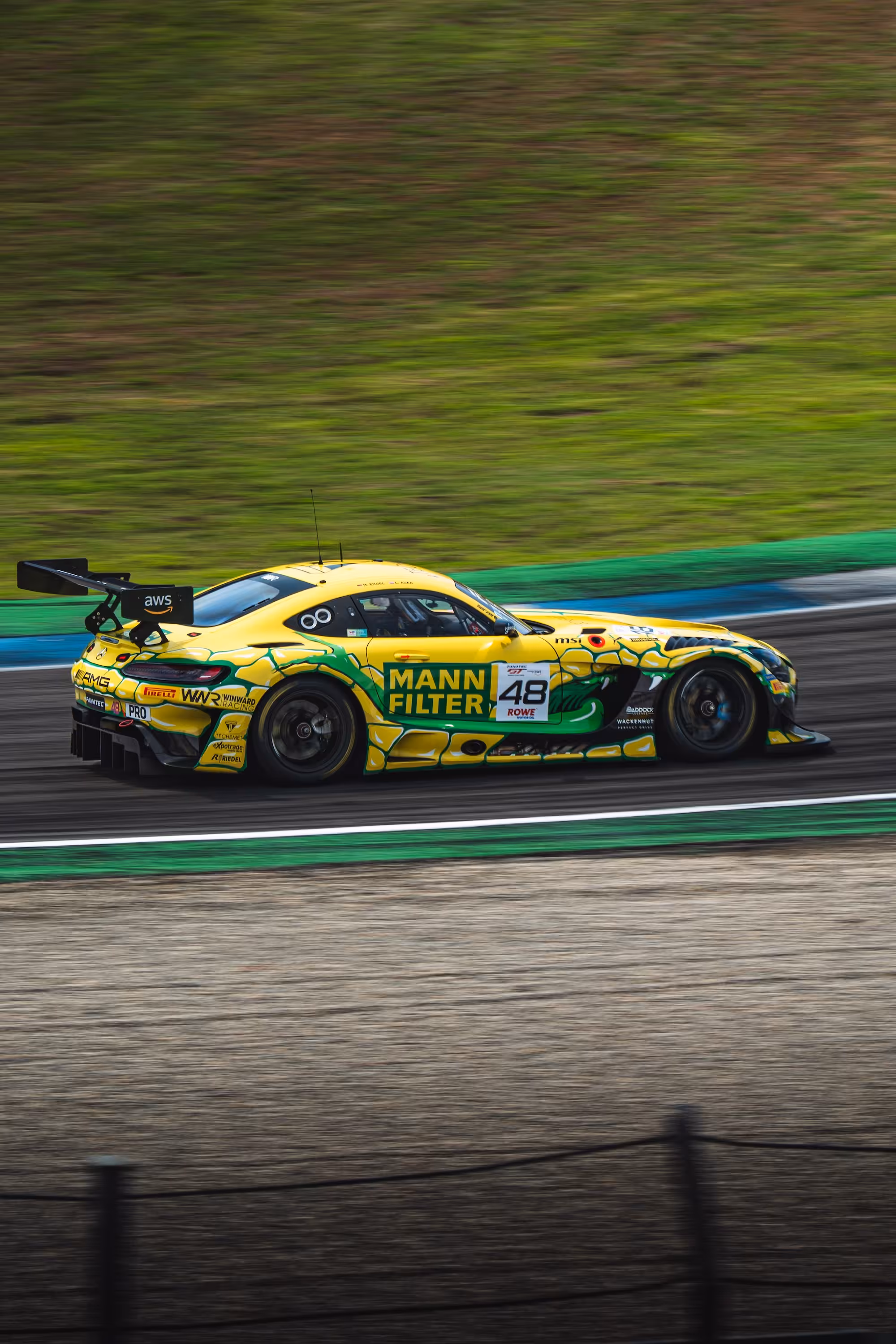 Der gelb-grüne Mercedes-AMG GT3 im Mamba-Design von MANN-FILTER rast über die Rennstrecke des Hockenheimrings. Das Auto mit der Startnummer 48 ist in dynamischer Seitenansicht vor grünem Rasen zu sehen.