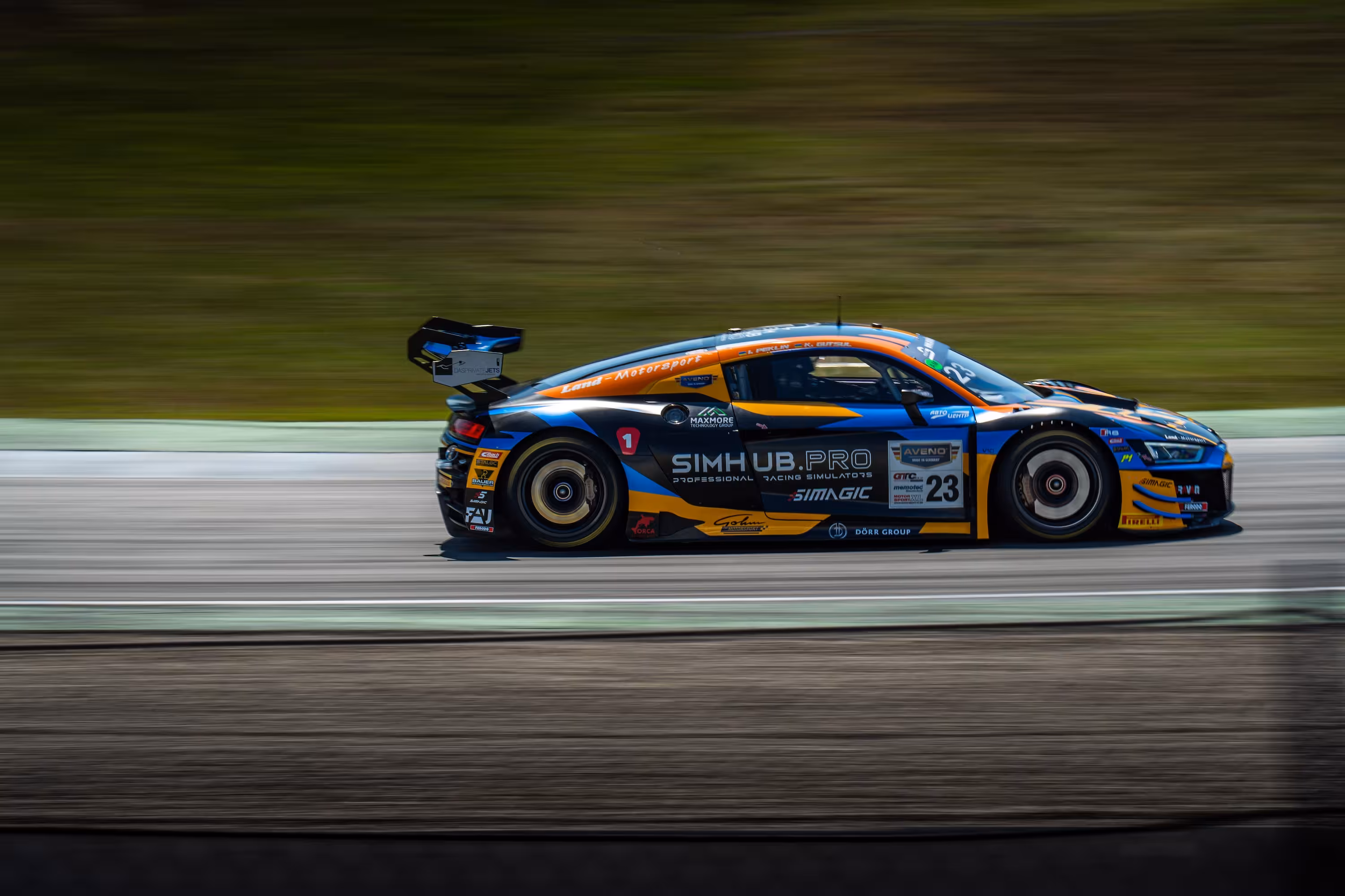 Seitenansicht eines Audi R8 LMS in voller Fahrt auf dem Hockenheimring. Der Rennwagen (Nr. 23) mit einem blau-orange-schwarzen Design mit Simhub.pro-Werbung. Durch die Geschwindigkeit wirkt der grüne Hintergrund stark verwischt.