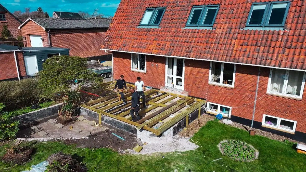 Hold af tømrere bygger terrassefundament i træ foran hus.