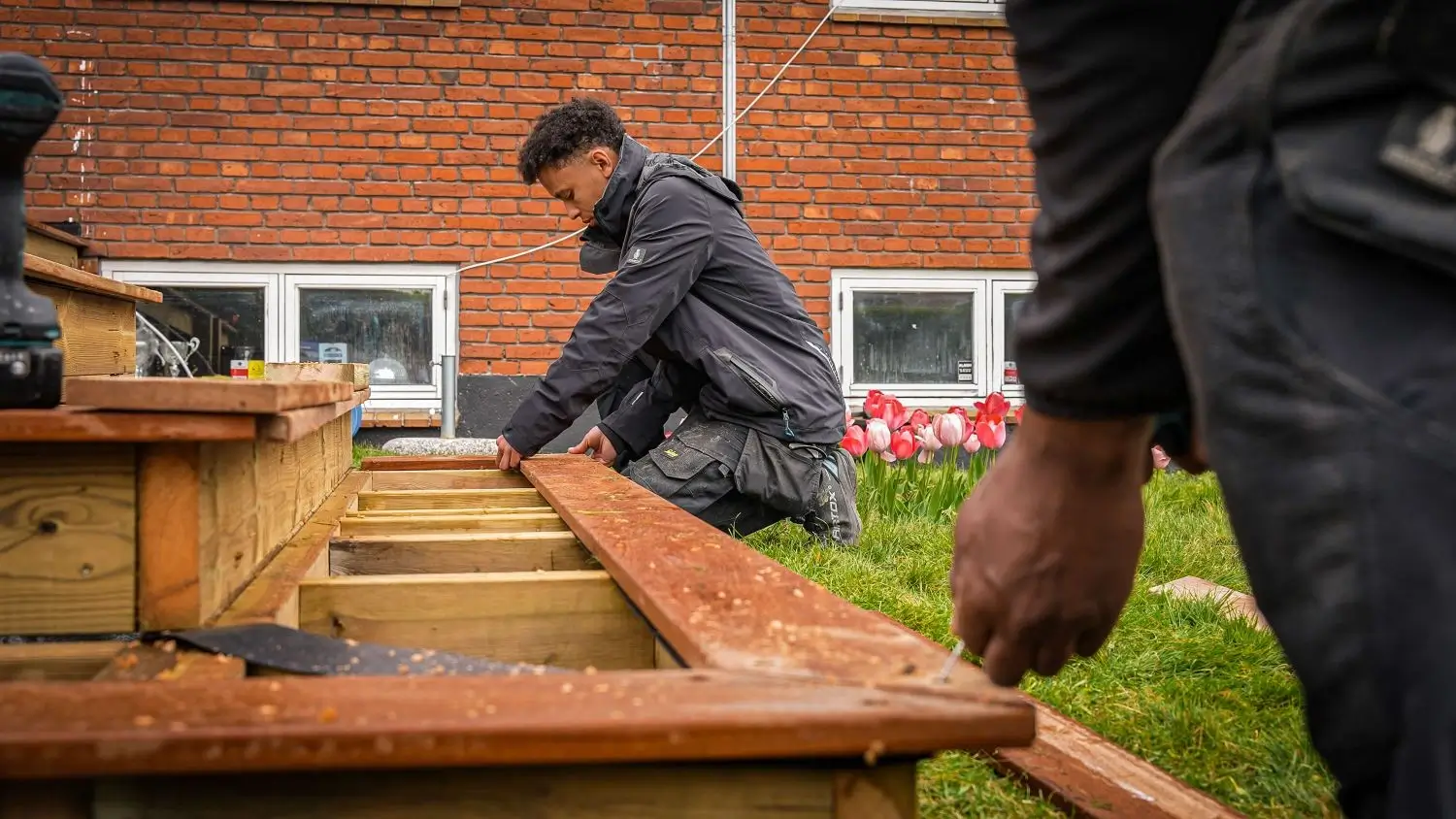 Tømrer arbejder med montering af træbrædder på ny terrasse foran murstenshus