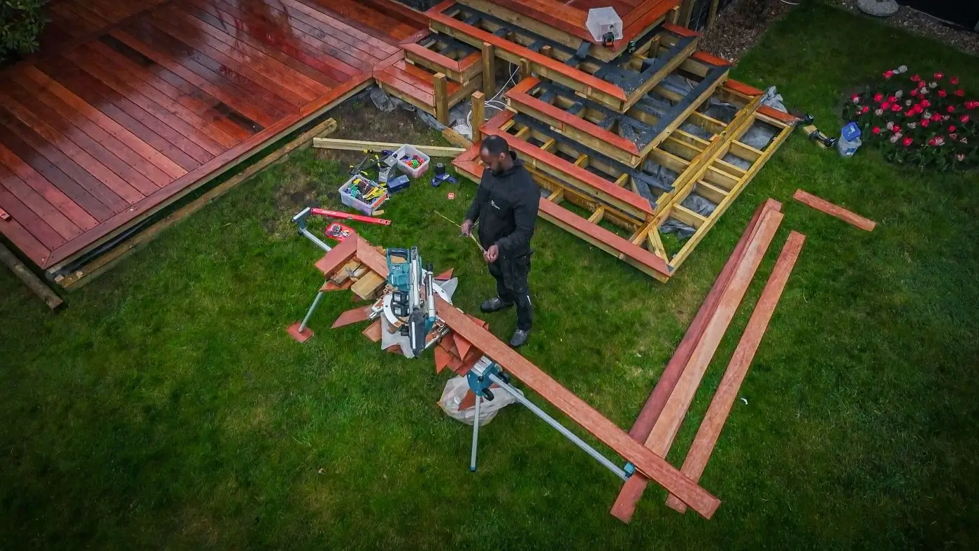 Set fra oven står tømrer og måler og saver træbrædder til opbygning af ny terrasse i have