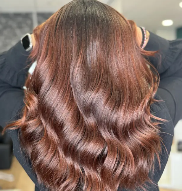 Femme de dos avec un balayage cuivré sur cheveux brun, long et ondulé. 