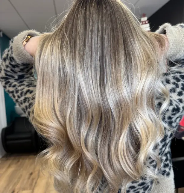 Femme de dos avec un balayage blond cendré sur cheveux blonds, longs, apportant des reflets froids et une profondeur élégante.

