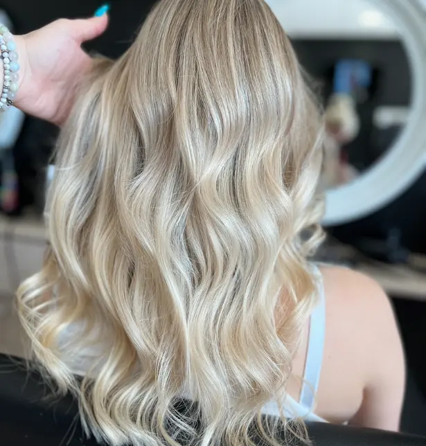 Femme de dos avec un balayage blond polaire sur base blonde, cheveux longs,  offrant un fini lumineux et très froid.