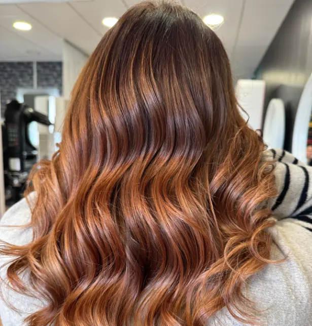 Femme de dos avec un balayage cuivré sur cheveux longs et ondulés. 