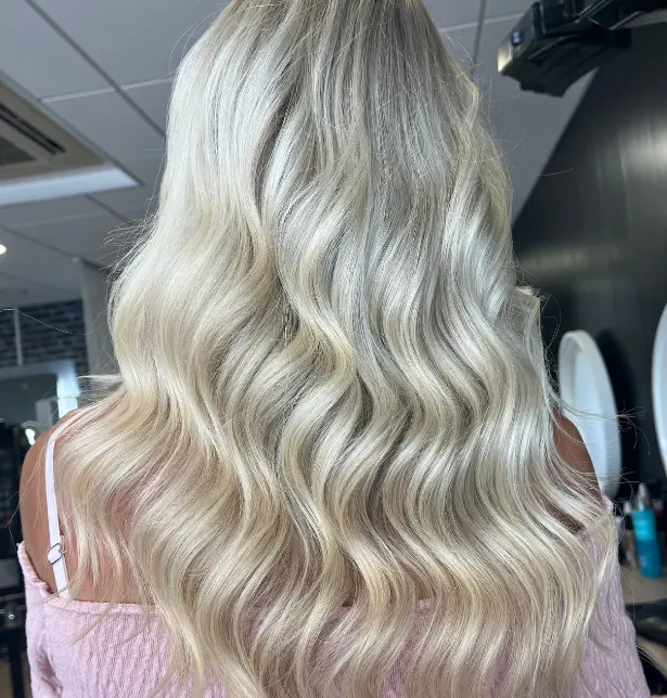 Femme de dos avec un balayage blond argenté tendance sur cheveux longs et ondulés