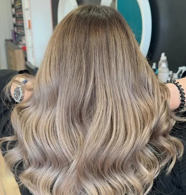 Femme de dos avec un balayage blond beige sur cheveux longs réalisé à l'atelier des embellis.