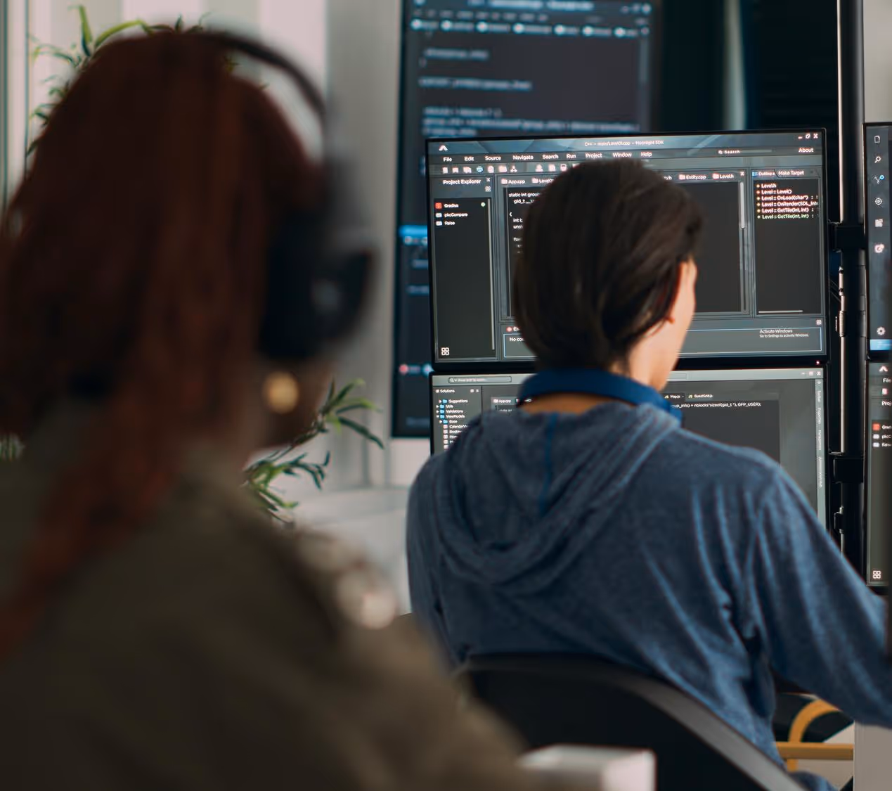 Two software developers working at desks with multiple monitors displaying code.