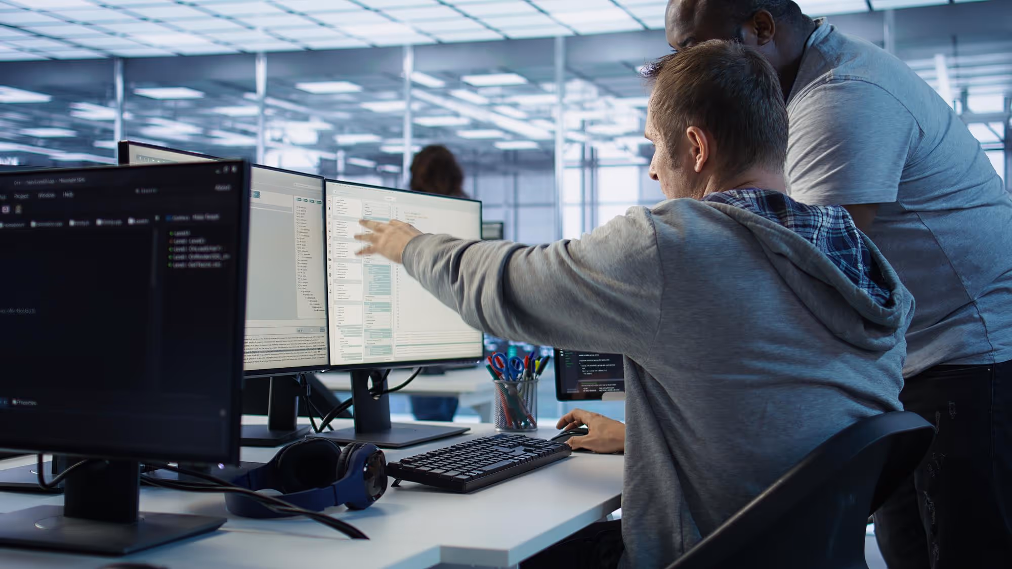 Two men collaborate on a project while looking at multiple computer monitors in a modern office.